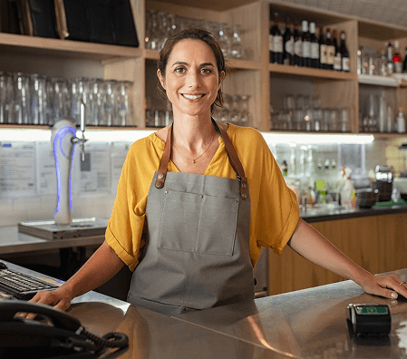 Dona de estabelecimento comercial sorrindo atrás do balcão.